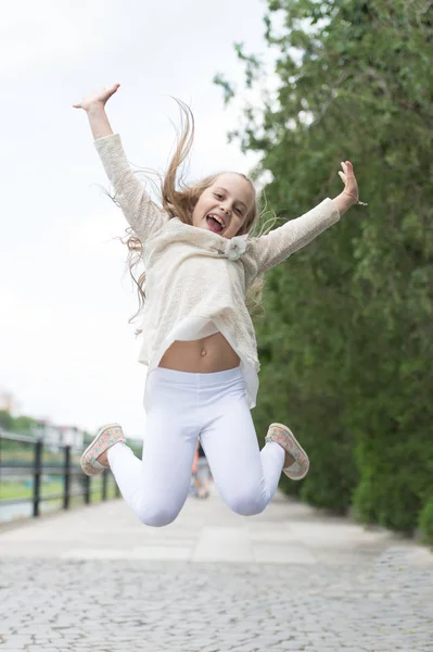 Flicka på glad leende ansikte, natur på bakgrunden. Lycka koncept. Ung flicka med glada uttryck hoppa på internationella barnens dag. Barn glad och glad njuta av promenad i parken — Stockfoto