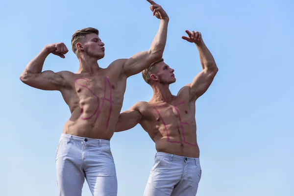 Mannen gespierd met naakt sexy torso, sky op achtergrond. Atleten met inscriptie verkoop op gespierde borst. Verkoop concept. Atleten op ernstige gezichten te tonen van de kracht en de macht van hun spieren — Stockfoto