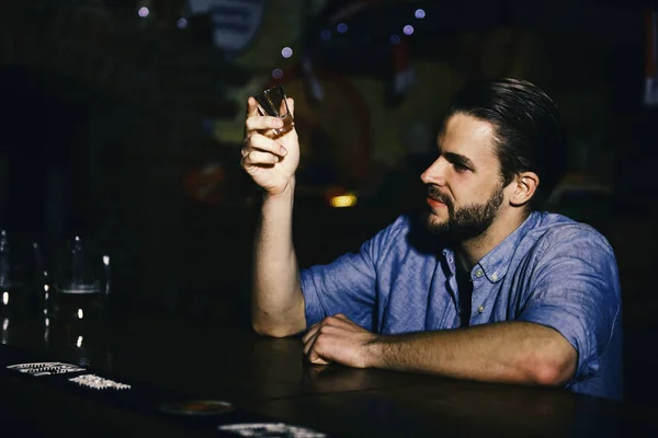 Alcohol addiction, loneliness. man sits in bar with empty shot glass in hand.