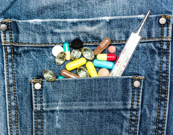 口袋里用五颜六色的药丸和水银温度计作为医学胸的多样性的象征。药片或药片散落在牛仔裤上, 牛仔布的背景。医学胸口概念 — 图库照片