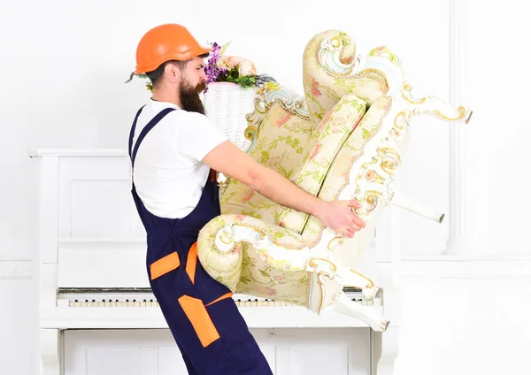 Zijaanzicht sterke bebaarde man uitvoering van oude fauteuil voor piano. Verhuizer wandelen met broze oude stuk van het meubilair in zijn handen. Verplaatsen naar nieuwe plek — Stockfoto