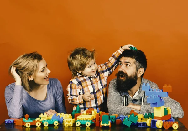 Happy family play. Family with cheerful faces build out of colored construction blocks