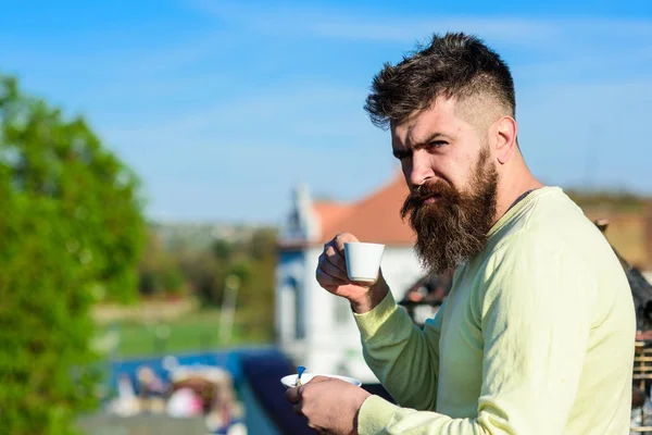 Hombre barbudo con taza de café expreso, bebe café. Hombre con barba y bigote en cara estricta bebe café, fondo urbano, desenfocado. Concepto de pausa. El hombre con barba larga se ve estricto y serio — Foto de Stock