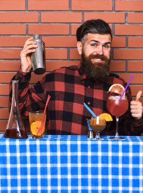 Alkollü içecekler kavramı. Tuğla duvar arka plan üzerinde kareli gömlekli adam içki hazırlar. Barmen uzun sakal ve bıyık ve mutlu yüz tutan shaker, şık saç ile alkollü kokteyl yapar