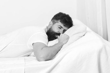 Günaydın. Yatakta, arka plan üzerinde beyaz duvar döşeme tişörtlü adam. NAP ve siesta kavramı. Adam beyaz yastık uyku sırasında başparmak emme