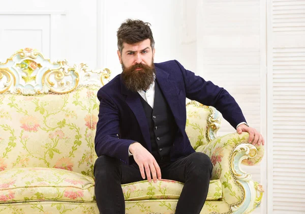 Концепция мужественности. Мужчина с бородой и усами в классическом костюме, стильном модном наряде. Мачо привлекателен и элегантен на серьезном, красивом лице, сидящем на старомодном роскошном диване — стоковое фото