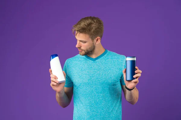 Man on thoughtful face chooses shampoo, violet background. Guy with bristle holds two bottles with shampoo, copy space. Man hesitates while making alternative decision. Hair care and shampoo concept — Stock Photo, Image