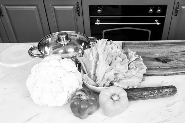 Cacerola y coliflor, pimientos, pepino, hojas de ensalada en la mesa de la cocina —  Fotos de Stock