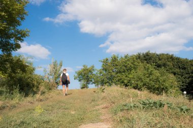 Adam sırt çantası ile güneşli günde tepe üzerinde yürür. Hiking kavramı. Yolcu sırt çantası yürüyüş dağlar, mavi gökyüzü arka plan ile. Adam doğa aşığı zevk yaz'da dağlarda yürüyüş