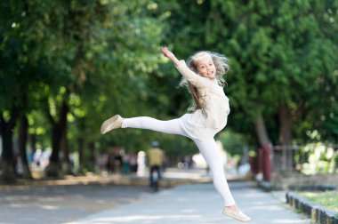 Çocuk mutlu ve neşeli parkta yürüyüş tadını çıkarın. Mutluluk kavramı. Neşeli ifade ile çocuk jimnastikçi kadar uluslararası çocuk günü üzerinde atlar. Kız mutlu güler yüz üzerinde atlar, doğa üzerinde arka plan
