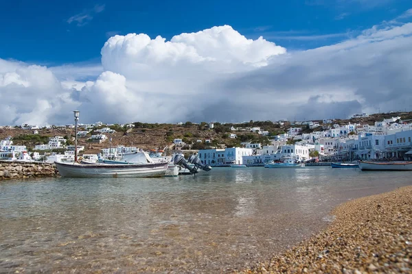 Mykonos, Greece - May 04, 2010: sea beach with boats on cloudy blue sky. Houses on mountain landscape by sea. Mediterranean architecture and design. Summer vacation on island. Wanderlust and travel — Stock Photo, Image
