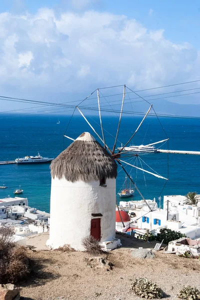 Windmill by sea in Mykonos, Greece. Windmill on mountain landscape cloudy sky. Whitewashed building with sail and straw roof with nice architecture. Summer vacation on island. Landmark and attraction
