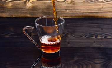 Sıvı sıçraması ve su damlaları ile dökme çay bardak. Su veya çay sıçraması ile koyu ahşap arka plan üzerine dökülen Kupası. Bira çay kavramı