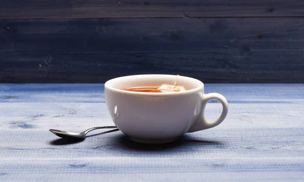 Becher gefüllt mit heißem Wasser und Tauchbeutel mit schwarzem Tee. Prozess des Aufbrühens von Schwarztee im Becher. Becher gefüllt mit kochendem Wasser, Teebeutel und Löffel auf blauem Holz Textur Hintergrund. Teegebräu-Konzept — Stockfoto