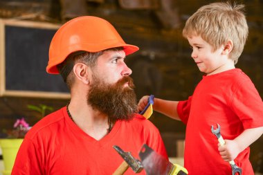 Baba, üst koruyucu kask okul atölyesinde farklı araçları kullanmak için küçük oğlu öğretim içinde sakallı. Babalık kavramı. Evlat, çocuk neşeli anahtar anahtarı, baba ile öğrenme kullanım araçları tutar