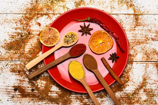 Mutfak konsepti. Baharat tüm ahşap yüzey üzerinde dağınık. Tabak ve kaşık Beyaz ahşap zemin üzerinde kurutulmuş portakal ve serin biber ile. Öğütülmüş kırmızı biber ve dağınık curcuma toz baharat