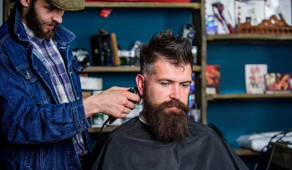 Barbeiro com cortador de cabelo funciona no penteado para barbearia barba cara fundo. Conceito de estilo de vida Hipster. Barbeiro com clipper aparar o cabelo na nuca do cliente. Hipster cliente recebendo corte de cabelo — Fotografia de Stock