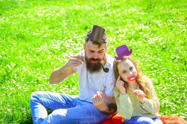 Aristocrates kavramı. Aile açık havada eğlence harcamak. Baba ve kızı, grassplot, arka planı yeşil çimenlerin üzerinde oturur. Çocuk ve babası silindir şapka, dudaklar ve boru photo booth öznitelikleri ile poz