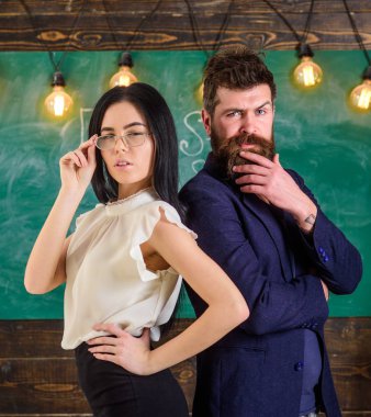 Sakal ve gözlük stand sırt sırta, kara tahta arka plan öğretmen olan adam. Öğretmen ve öğretmen rahat görünüyor. Ekip çalışması kavramı. Bayan ve birlikte okulda çalışan hipster