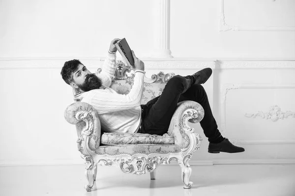 Concepto inteligente. Macho smart pasa el ocio con el libro. Hombre con barba y bigote se sienta en el sillón y lee libro, fondo blanco de la pared. Científico, profesor de cara tranquila explora la literatura —  Fotos de Stock