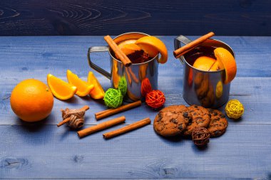 Alkollü kokteyl kavramı. Saflık çelik kupalar ve baharat eski ahşap masa üzerinde mulled şarap. Kupalar mulled şarap veya tanımlama karanlık mavi zemin üzerine yakın sıcak elma şarabı ile. Portakal dilim yakınındaki mulled şarap