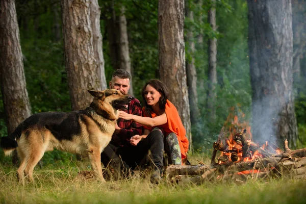 Paar mit Schäferhund am Lagerfeuer, Naturhintergrund. — Stockfoto