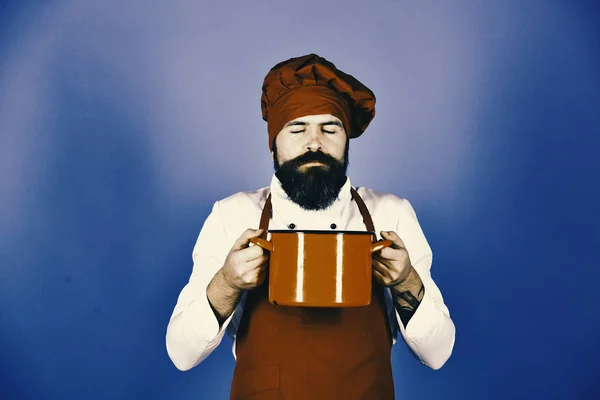 Chef-kok met rode braadpan of pan. Man met baard houdt keukengerei op blauwe achtergrond. — Stockfoto