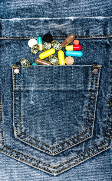 医学胸的概念。口袋里用五颜六色的药丸作为医学胸的多样性的象征。散在牛仔裤上的药片或药片, 牛仔布背景 — 图库照片