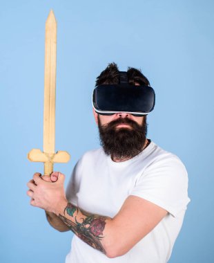 Oyun kavramı. Hipster ciddi bir yüz üzerinde sanal gerçeklik oyun oyun keyfini çıkarın. Adam kafa monte ekran ile kılıç tutan, dövüş Vr gözlük, açık mavi renkli sakallı Vr. adam oyunu oyna