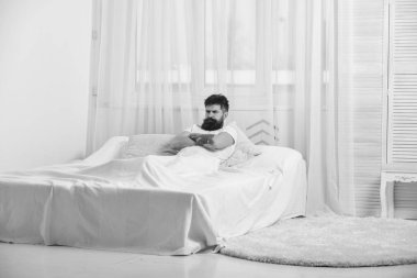 Günaydın. Yatak, arka plan üzerinde beyaz perde döşeme tişörtlü adam. Mutsuz ciddi yüz adam sabah kızgın görünüyor. Maço sakal tutun eliyle göğsüne rahatlatıcı geçti. Kötü ruh kavramı