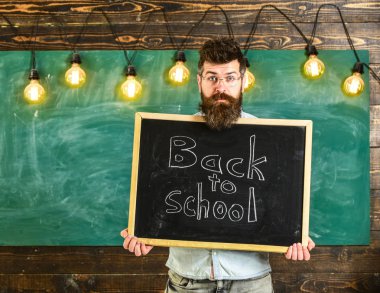 Öğretmen sürpriz yüzündeki blackboard ile başlık okula geri tutar. Sakallı öğrenciler, arka plan kara tahta ağırlamaktadır. Öğretmen kara tahta dışarı bakmak. Öğretim yılı konsept başlangıcı