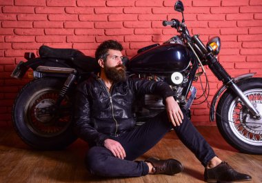 Sakallı, motorcu motorlu bisiklet garaj, tuğla duvar arka plan yakınındaki deri ceketli adam. Yenilikçi, vahşi Motorcu deri ceketli dalgın yüzündeki motosiklet yakın yerde oturamaz. Vahşi motorcu kavramı
