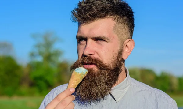 Concept de dent sucrée. Homme barbu avec un cône de crème glacée. Homme avec barbe et moustache sur le visage calme mange de la crème glacée, morsure cône de gaufre, fond bleu ciel, déconcentré. Homme à longue barbe profiter de la crème glacée — Photo