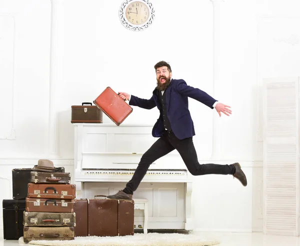 Macho attraktiva och eleganta på glada ansikte bär vintage resväskor, hoppning. Mannen med skägg och mustasch i kostym bär bagage, lyx vit interiör bakgrund. Efterlängtade semester koncept — Stockfoto