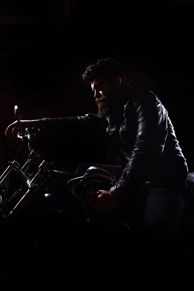 Conceito de piloto nocturno. Macho, motociclista brutal em jaqueta de couro andar de moto à noite, espaço cópia. Homem com barba, motociclista em jaqueta de couro sentado na moto do motor na escuridão, fundo preto — Fotografia de Stock