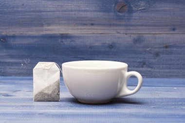 Çay zaman kavramı. Fincan ya da beyaz Porselen Kupa şeffaf sıcak su ve çay torba ile. Kupa su ve çay poşeti mavi ahşap zemin üzerine kaynar ile dolu. Süreç içinde seramik kupa demleme çay