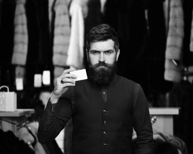 Sakal ve kartvizit adam. Boş kağıt ile iş adamı. Adam kendinden emin yüz defocused kürklü Mont raflar arka planda, kartta bulunur. Finans ve alışveriş kavramı.