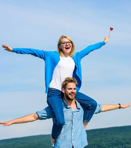 Freedom concept. Couple in love enjoy feeling freedom outdoor sunny day. Man carries girlfriend on shoulders, sky background. Couple happy date having fun together. Lovers enjoy date and feeling free