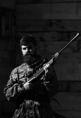 Avcı kavramı. Sakallı kamuflaj elbiseler, ahşap iç arka plan giyer. Maço gamekeepers evinde sıkı yüzünde. Hunter, silahla acımasız hipster hazırlamak tüfek avcılık için kopya alanı