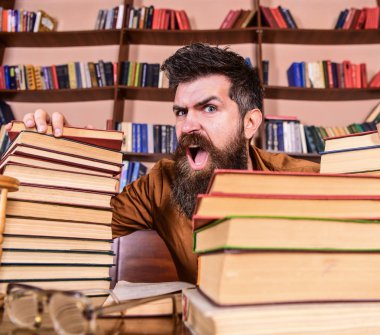 Öğretmen ya da öğrenci sakallı defocused gözlük ile masada oturur. Çılgın bilim adamı kavramı. Yüz Kitaplığı'nda, eğitim sırasında kitaplar, kitap rafı arka plan üzerinde yığınları arasında bağıran adamın