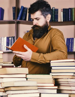 Adam meşgul düşünceli yüz kitap okumak, kitap rafı arka plan üzerinde. Eğitim ve bilim kavramı. Öğretmen veya kitaplığındaki kitap yığınları arasında sakal eğitim ile öğrenci