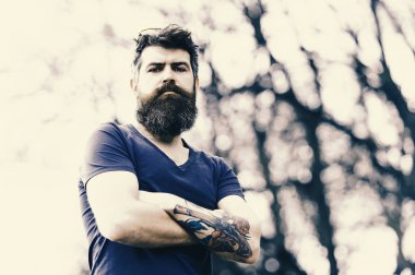 Silah ve gül ile acımasız sakallı adam kollarını göğsüne çarpı işareti ile ayakta dövme. Yakışıklı adam mavi gözleri ve açık havada poz güzel saç modeli