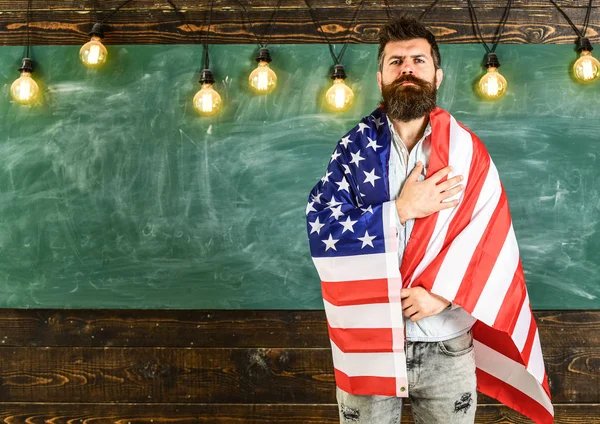 Conceito de educação patriótica. Professor americano coberto com bandeira americana. Homem com barba e bigode no rosto sério com bandeira dos EUA, quadro-negro no fundo. Professor ensina a amar a pátria, EUA — Fotografia de Stock