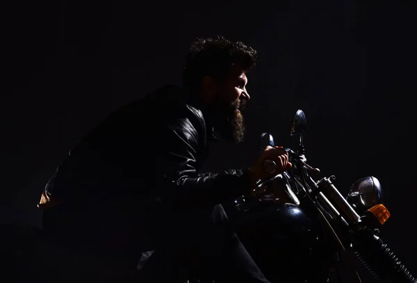 Mannen med skägg, biker i skinnjacka sitter på motorcykel i mörker, svart bakgrund. Manlighet koncept. Macho, brutal biker i läder jacka Rider motorcykel nattetid, kopia utrymme — Stockfoto