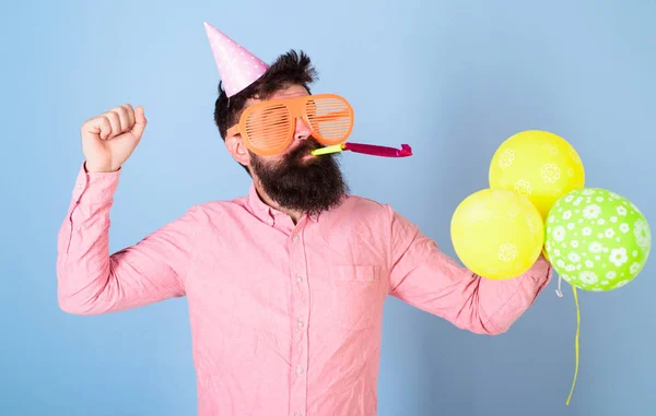 开朗的大胡子男子在生日帽吹党哨子, 有趣的时间, 幸福的概念。艺术家在大疯狂的眼镜持有彩色气球。男子与时髦的胡子和胡子庆祝 — 图库照片