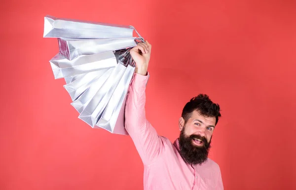 Guy shopping on sales season with discounts. Man with beard and mustache holds shopping bags, red background. Hipster on happy face is shopping addicted or shopaholic. Shopping concept — Stock Photo, Image