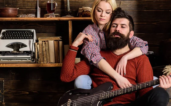 Señora y hombre con barba en caras de ensueño abrazos y toca la guitarra. Pareja en madera vintage interior disfrutar de la música de guitarra. Pareja enamorada pasar una velada romántica en un ambiente cálido. Concepto romántico de noche — Foto de Stock