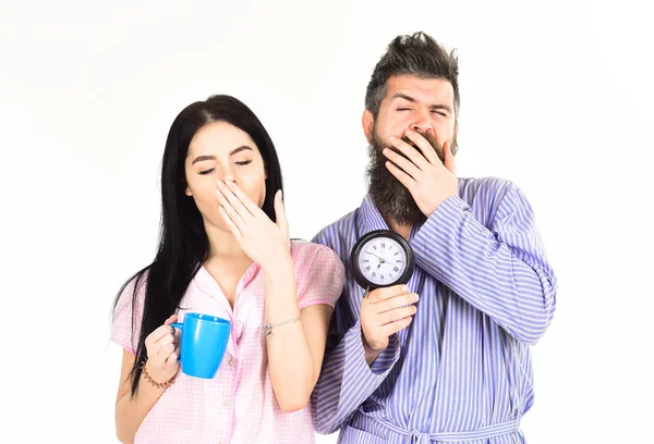 Concept matinal parfait. Fille avec tasse de café, homme tenir horloge dans la main et bâiller. Couple se réveilla tôt le matin. Couple amoureux, jeune famille en pyjama, peignoir isolé sur fond blanc — Photo