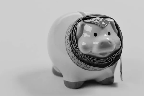 Saving money. Ceramic toy pig with blue flexible ruler on yellow background — Stock Photo, Image