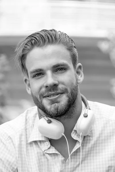 Man face. Handsome unshaven and young smiling man with headphones listening music outdoor on sunny day. Guy with headphones on neck.